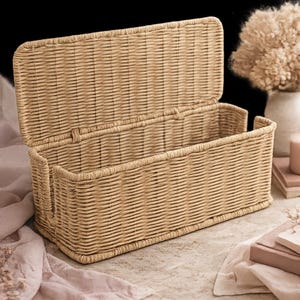 May include: A rectangular woven wicker storage basket with a hinged lid, open to reveal the interior. The basket is a light tan color and appears to be made of natural materials. The lid is slightly ajar, and the basket sits on a neutral surface.