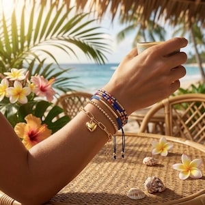 May include: A stack of four bracelets worn on a wrist. The set includes a gold-tone chain bracelet with a heart charm, a gold-tone beaded bracelet, a solid gold-tone bar bracelet, and a multi-colored beaded bracelet with blue, red, and gold tones.