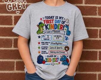 May include: A sport grey t-shirt featuring a colorful graphic for the first day of kindergarten. The design includes dinosaurs, a baseball, a backpack, and an apple, with text fields for name, age, height, career goals, interests, and school year.