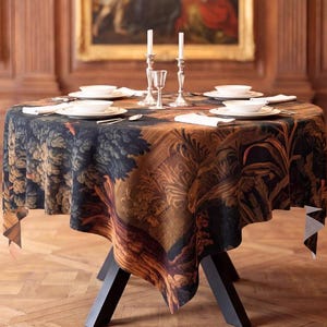 Peut inclure: Une table à manger ronde recouverte d'une nappe sombre de style tapisserie avec un imprimé paysage. La table est dressée avec des assiettes blanches, des couverts en argent, des serviettes blanches et deux bougeoirs en argent avec des bougies blanches.