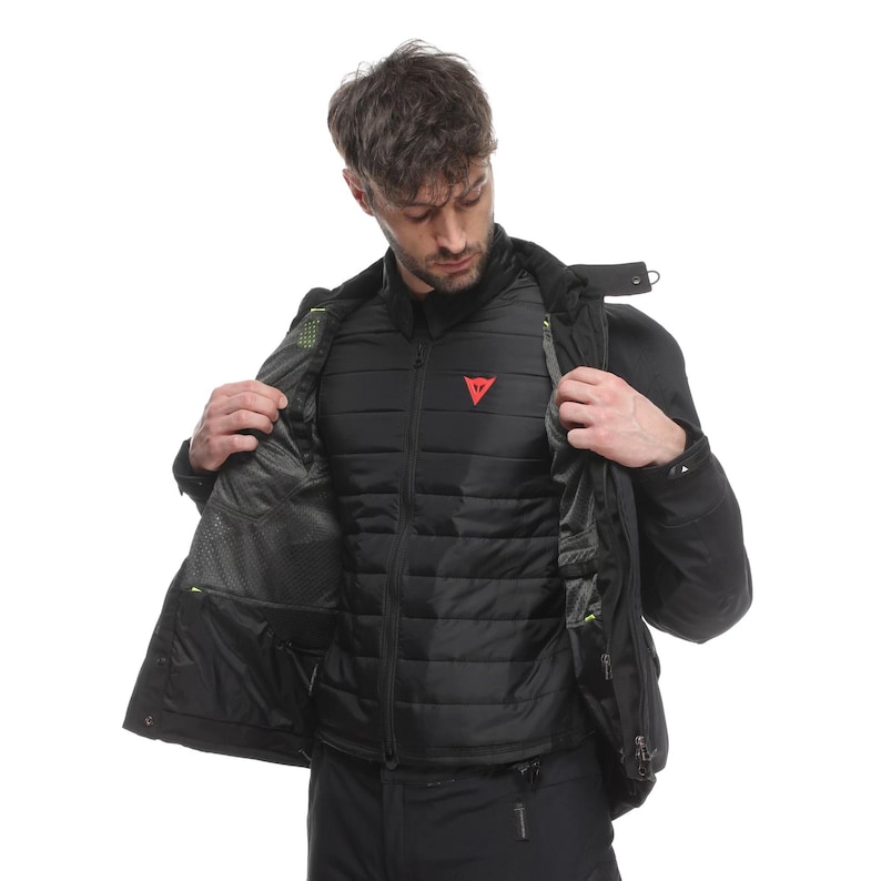 May include: Black motorcycle jacket with a quilted inner layer and a red logo on the chest. The jacket has multiple pockets and a high collar. The model is wearing black trousers.