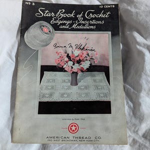 May include: Vintage "Star Book of Crochet" booklet. The cover features a floral arrangement in a vase, a crocheted tablecloth, and a ball of yarn. The text reads "Star Book of Crochet Edgings-Insertions and Medallions" and "American Thread Co."