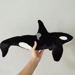 May include: A plush orca whale toy, featuring a black and white color scheme. The toy has a dorsal fin, flippers, and a tail. The orca has white patches around the eyes and on the belly. The toy is soft and cuddly.