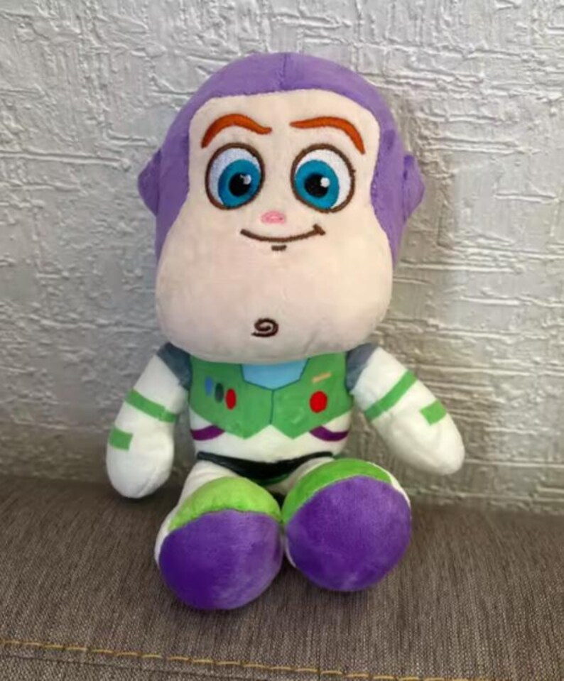 May include: A plush Buzz Lightyear toy from the Toy Story franchise. The toy features a purple head, a white face, and a green and white space suit. The toy has large blue eyes and is sitting down.