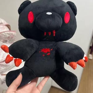May include: A black plush bear with red eyes, claws, and a blood-like stain on its chest. The bear has a menacing expression, with sharp teeth and claws. The plush toy is soft and cuddly, but with a dark, edgy aesthetic.