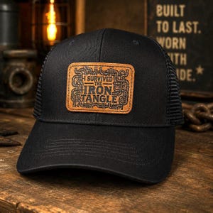 May include: A black trucker hat featuring a rectangular tan leather patch on the front. The patch displays a complex pipe-like graphic design and the text I SURVIVED THE IRON TANGLE in black lettering. The hat has a solid front and mesh back.