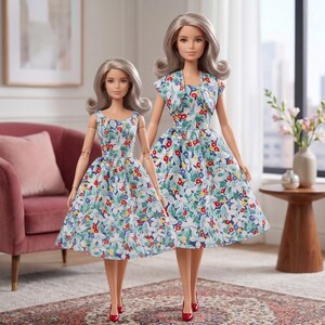 May include: Two dolls with shoulder-length silver hair, each wearing a sleeveless dress featuring a light blue background with a pattern of red, white, and green flowers and leaves. The taller doll also wears a matching cropped jacket over the dress.