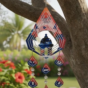 Puede incluir: Un adorno de viento decorativo con una parte superior en forma de diamante y colgantes de diamante más pequeños. La parte superior presenta colores rojo, blanco y azul con una silueta de un edificio. Los colgantes tienen varios diseños y están conectados con cuentas transparentes.