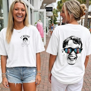 Könnte beinhalten: Ein weißes kurzärmeliges T-Shirt mit einer schwarzen Grafik auf der Brust, die eine Hand in L-Form zeigt, mit dem Text L7 WEENIE darüber. Auf der Rückseite des Shirts befindet sich ein großes schwarz-weißes Porträt eines lachenden Kindes mit Sonnenbrille.