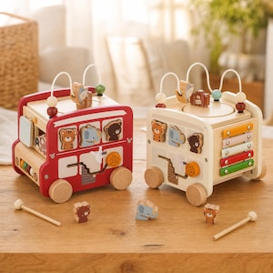 May include: Two wooden activity bus toys, one red and one cream, featuring animal-shaped sliding pieces, a bead maze on top, and a colorful xylophone on the side of the cream bus. Each bus has wooden wheels and comes with a small wooden mallet.