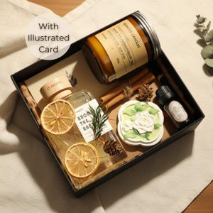 Könnte beinhalten: Schwarze Geschenkbox mit Aromatherapie-Artikeln. Enthält eine Kerze, ätherisches Öl, eine Parfümflasche mit getrockneten Zitronenscheiben, eine dekorative Blumenseife und Zimtstangen. Die Box trägt den Text "With Illustrated Card".