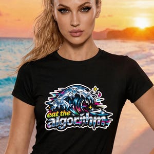 May include: Black t-shirt featuring a colorful graphic of a wave with the text "eat the algorithm". The design includes shades of blue, pink, and yellow. The shirt is short-sleeved.
