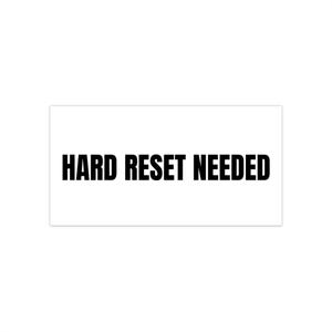 May include: A white rectangular sticker with the words "HARD RESET NEEDED" in bold, black capital letters. The text is centered on the sticker, which has a clean, minimalist design.