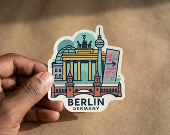 May include: A die-cut sticker featuring a stylized illustration of Berlin landmarks including the Brandenburg Gate, the TV Tower, and a bridge. The design uses a palette of teal, yellow, and terracotta, with the text BERLIN GERMANY printed at the bottom.