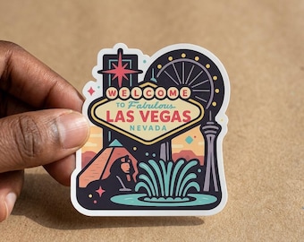 May include: A die-cut vinyl sticker featuring a stylized graphic of the Welcome to Fabulous Las Vegas Nevada sign, a pyramid, a sphinx, a fountain, and a Ferris wheel in a color palette of dark blue, light blue, yellow, and coral pink.
