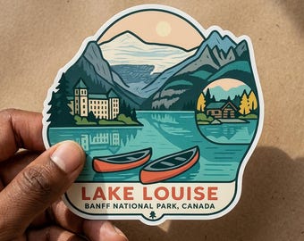 May include: A die-cut sticker featuring a landscape illustration of Lake Louise in Banff National Park, Canada. The design shows two orange canoes on turquoise water, a large hotel, mountains, and a small cabin. The text reads LAKE LOUISE BANFF NATIONAL PARK, CANADA.