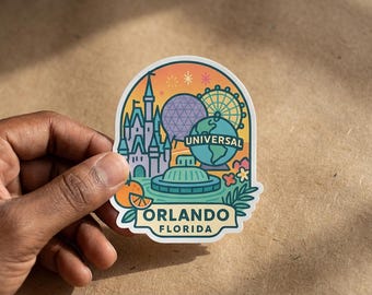 May include: A die-cut sticker featuring a colorful illustration of Orlando, Florida landmarks including a castle, a geodesic dome, a Ferris wheel, and a globe with the text UNIVERSAL, ORLANDO, FLORIDA, accented by an orange slice and tropical foliage.