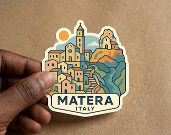May include: A die-cut sticker featuring a stylized illustration of the city of Matera, Italy. The design displays yellow buildings, a tall bell tower, a sun, and a blue landscape. The text MATERA ITALY is printed in bold dark blue letters at the bottom.