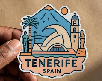 May include: A die-cut sticker featuring a stylized illustration of Tenerife, Spain. The design includes a mountain, a palm tree, a building with a tower, and a wave, with the text TENERIFE SPAIN printed in dark blue on a light peach background.
