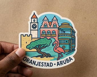 May include: A die-cut sticker featuring a colorful illustration of Oranjestad, Aruba. The design includes a clock tower, a pink building, a yellow wall, a green tree, a pink flamingo, and a blue trolley car, with the text ORANJESTAD ARUBA below.