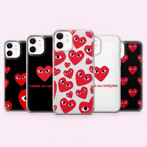 May include: Five phone cases with red heart graphics with eyes. The cases have a variety of designs, including a black case with a large red heart, a clear case with multiple red hearts, and a white case with a large red heart and text.