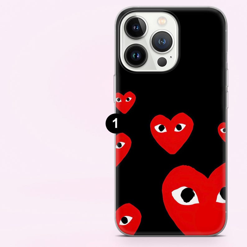 May include: Black phone case featuring a pattern of red hearts with white eyes. The case has a clear border and a camera cutout. The design is repeated across the back of the phone case.