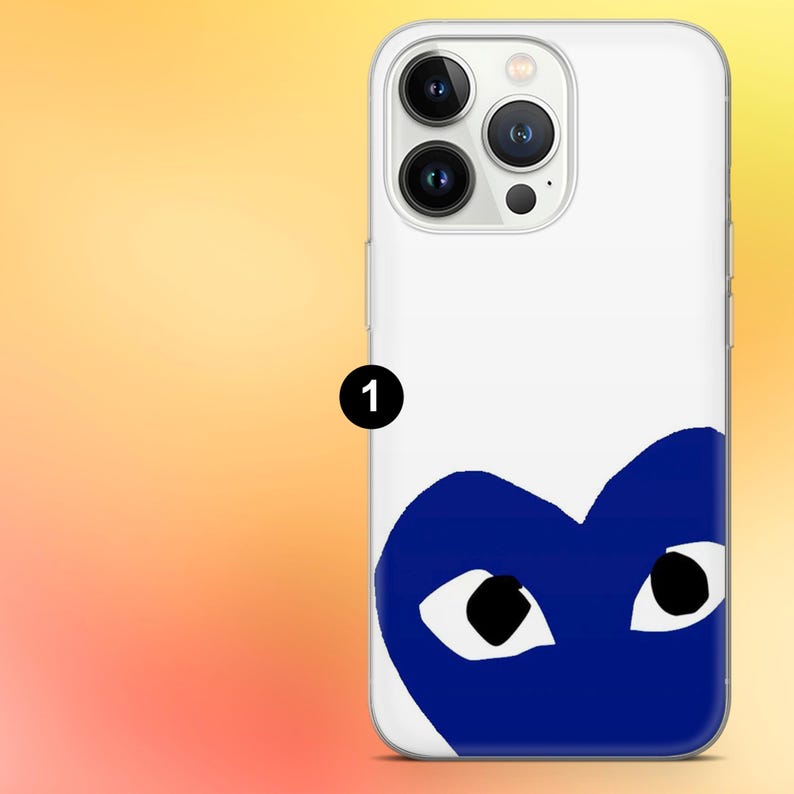 Op de afbeelding: Witte telefoonhoes met een blauw hartontwerp met zwarte ogen. De hoes heeft een transparante rand en is ontworpen voor een telefoon. De achtergrond is een gele en oranje gradi&euml;nt.