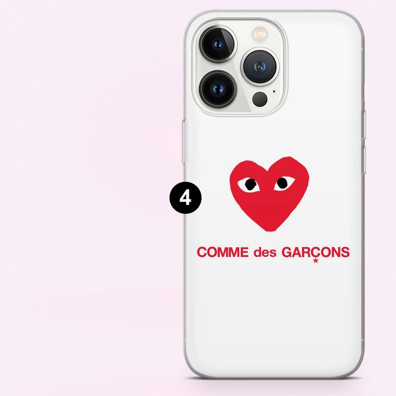 May include: White iPhone case featuring a red heart with eyes and the text "COMME des GAR&Ccedil;ONS" in red. The case has a clear border and covers the phone's back and sides.