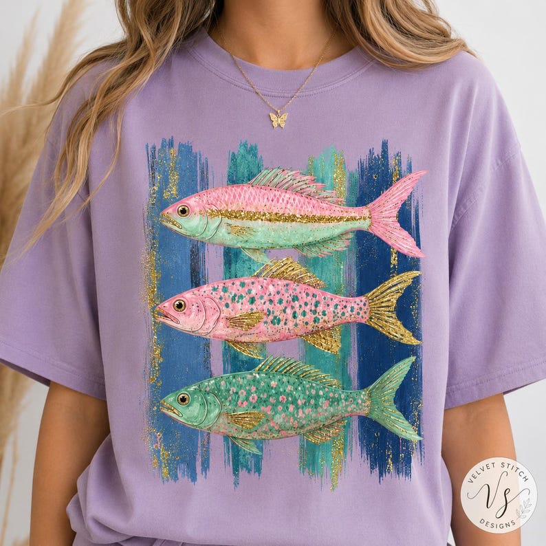 Pode incluir: Uma t-shirt roxo-claro com um gr&aacute;fico de tr&ecirc;s peixes empilhados verticalmente. Os peixes s&atilde;o representados em tons de rosa, verde e glitter dourado. Atr&aacute;s dos peixes, h&aacute; pinceladas verticais em tons de azul, turquesa e glitter dourado.