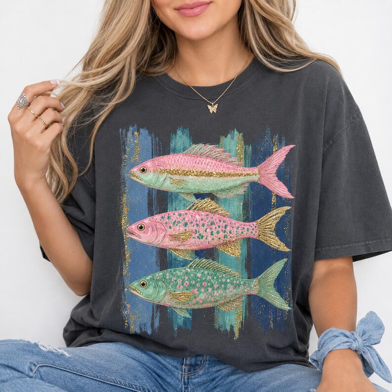 Pode incluir: Uma t-shirt cinzento-carv&atilde;o de manga curta com uma impress&atilde;o gr&aacute;fica de tr&ecirc;s peixes empilhados. O peixe de cima &eacute; cor-de-rosa com uma risca dourada, o do meio &eacute; cor-de-rosa com pintas douradas e o de baixo &eacute; verde com pintas cor-de-rosa.