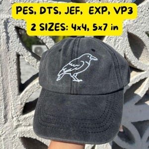 Puede incluir: Gorra de béisbol gris oscuro con un diseño de cuervo blanco bordado. La gorra tiene una visera curva y el texto "PES, DTS, JEF, EXP, VP3" y "2 TAMAÑOS: 10x10, 13x18 cm" en amarillo.