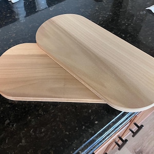 May include: Two oval-shaped wooden boards with a smooth, light-colored finish and visible layered plywood edges. The boards are stacked partially overlapping each other, showcasing a flat surface and rounded ends, crafted from natural light wood.