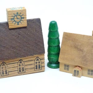 May include: Wooden toy village set featuring two houses, a green tree, and a clock tower. The houses have brown roofs and detailed window designs. The clock tower has a clock face design. A charming, nostalgic toy.