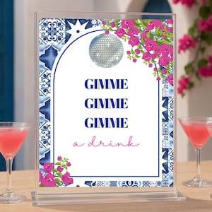 May include: A clear acrylic sign holder displaying a rectangular card with a blue and white tile border, pink bougainvillea flowers, a silver disco ball, and the text GIMME GIMME GIMME a drink in blue and pink lettering on a white background.