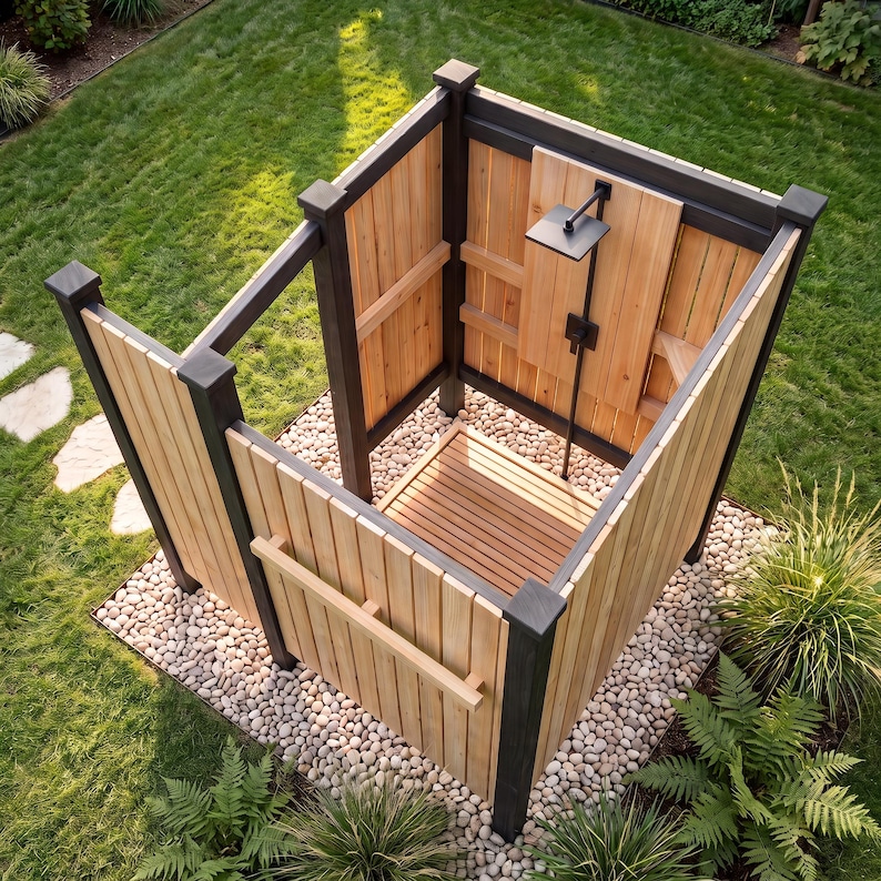 May include: An outdoor shower enclosure featuring vertical light-colored cedar wood planks framed by dark charcoal posts. The structure includes a slatted wood floor, a square matte black shower head, and a matching vertical pipe fixture.