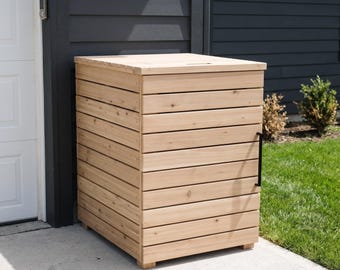 May include: A rectangular wooden storage enclosure featuring horizontal slats and a flat top lid. The structure is constructed from light-colored wood and includes a single vertical black metal handle attached to the front panel for access.