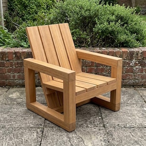 May include: A natural light brown wooden chair featuring a slatted backrest and a slatted seat. The chair is constructed with thick, square-profile wooden legs and armrests that form a continuous rectangular frame on each side of the seat.