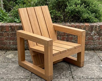 May include: A natural light brown wooden chair featuring a slatted backrest and a slatted seat. The chair is constructed with thick, square-profile wooden legs and armrests that form a continuous rectangular frame on each side of the seat.