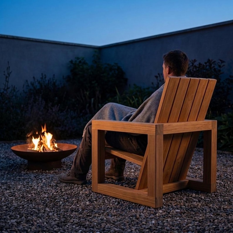 May include: A wooden outdoor chair with a slatted back and seat, featuring a boxy frame design. The chair is positioned next to a circular metal fire pit containing a burning fire with visible orange flames, set on a gravel ground surface.
