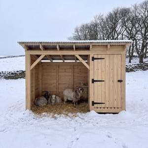 May include: A wooden animal shelter with a corrugated metal roof featuring icicles, an open-front section with straw bedding, and a closed storage compartment with a vertical plank door and black hinges, housing three goats in a snowy landscape.