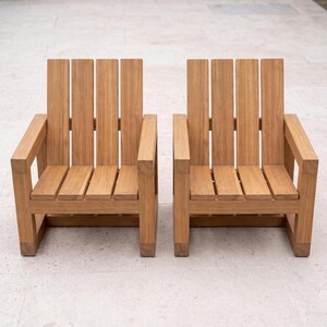 May include: Two matching armchairs constructed from light brown wood with a visible grain. Each chair features a high backrest composed of four vertical slats, a seat made of four horizontal slats, and two sturdy armrests supported by square legs.