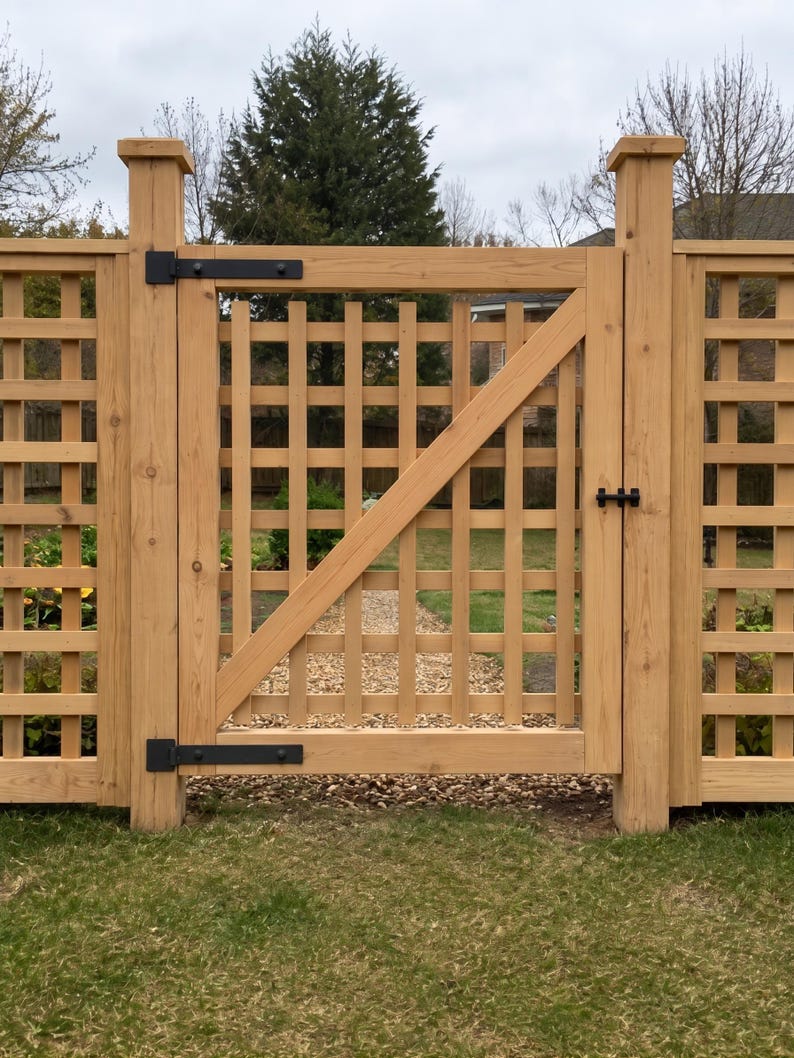 K&ouml;nnte beinhalten: Ein hellbraunes Holztorgartentor mit quadratischem Gittermuster und einer diagonalen St&uuml;tzstrebe. Das Tor ist zwischen zwei dicken Holzpfosten montiert und verf&uuml;gt &uuml;ber schwarze Metallscharniere sowie einen schwarzen Riegel.