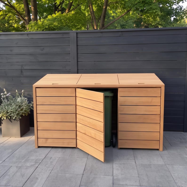 May include: A light brown wooden triple bin storage unit with horizontal slats and three hinged lids. The center door is open, revealing a green plastic waste bin inside. The structure features a clean, rectangular design with a natural wood finish.
