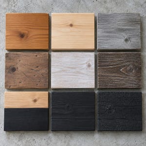 May include: A grid of nine rectangular wooden blocks featuring various finishes. The collection includes natural light wood, warm brown, weathered gray, dark brown, white-washed, solid black, charred black, and a two-toned block with natural and black.