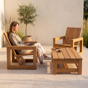 May include: Two light brown wooden armchairs with wide, flat armrests and slatted backrests, paired with a matching rectangular wooden coffee table. The furniture features a natural wood grain finish and a sturdy, block-style frame construction.
