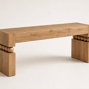 May include: A rectangular wooden bench with a light brown wood grain finish. The bench features a flat top surface supported by two thick, rectangular legs. Between the top and each leg are four spherical wooden beads arranged in a horizontal row.