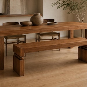 May include: A rectangular wooden dining table with thick legs and a matching wooden bench featuring decorative spherical accents between the seat and the base. The set is crafted from medium-toned wood with a visible grain, providing a sturdy surface.