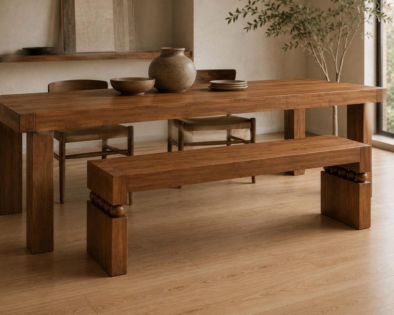 May include: A rectangular wooden dining table with thick legs and a matching wooden bench featuring decorative spherical accents between the seat and the base. The set is crafted from medium-toned wood with a visible grain, providing a sturdy surface.