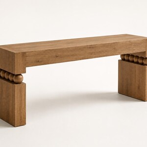 May include: A rectangular wooden bench with a flat top surface and two solid block legs. The bench features a row of four spherical wooden beads positioned horizontally between the top seat and each of the two vertical base supports.