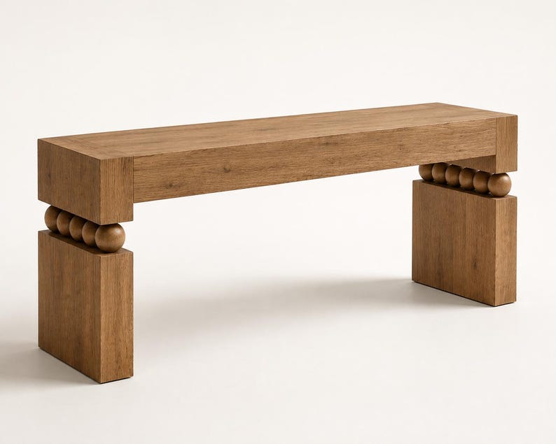 May include: A rectangular wooden bench with a flat top surface and two solid block legs. The bench features a row of four spherical wooden beads positioned horizontally between the top seat and each of the two vertical base supports.